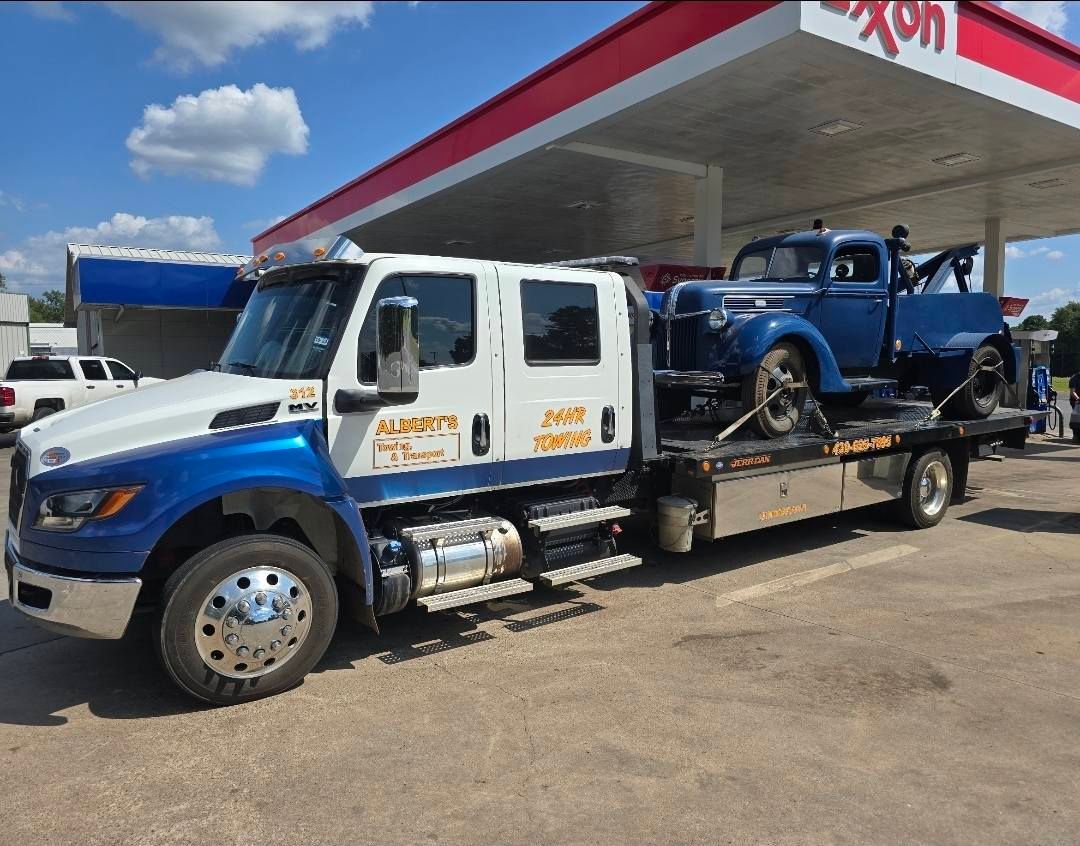 Tow truck, blue and white, loaded with a classic blue car at an Exxon gas station.