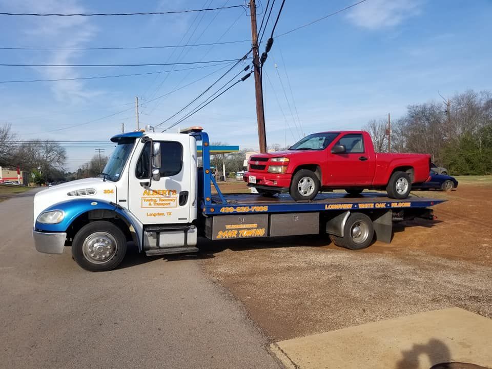 Tow truck carrying a red pickup truck on a road.