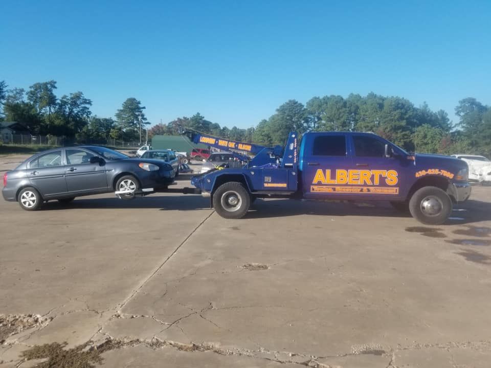 A blue tow truck from Albert's towing service towing a gray car on a paved lot.