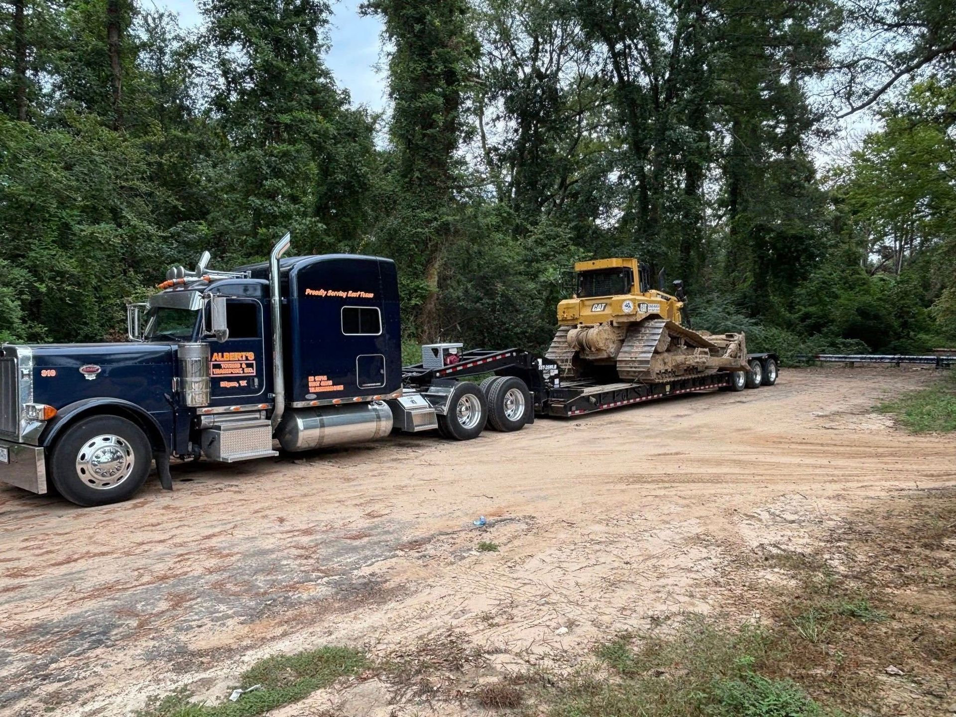 Blue semi-truck transports a yellow bulldozer on a trailer in a wooded area.