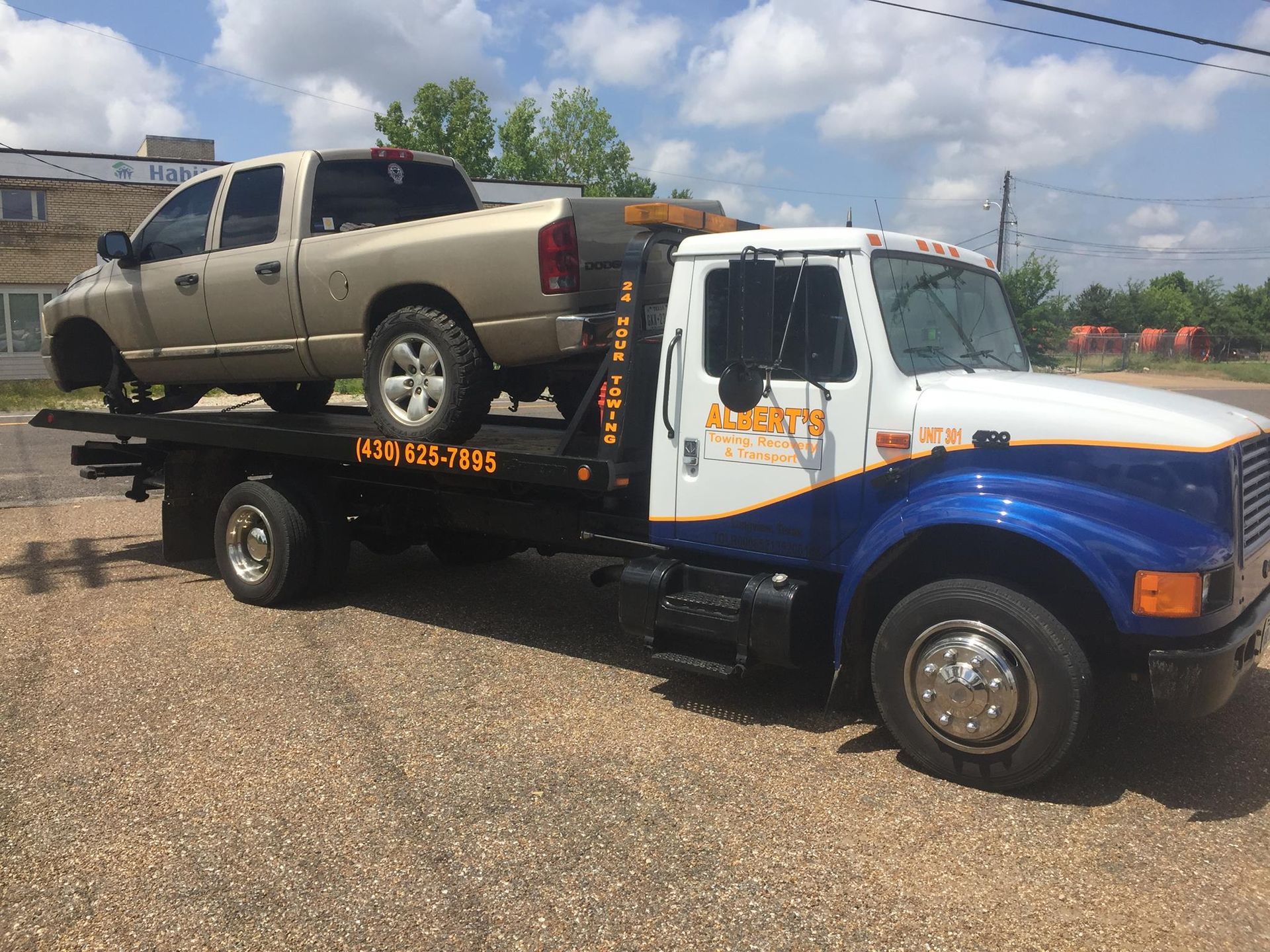 Tow truck with a beige pickup truck loaded on its flatbed, parked on gravel.