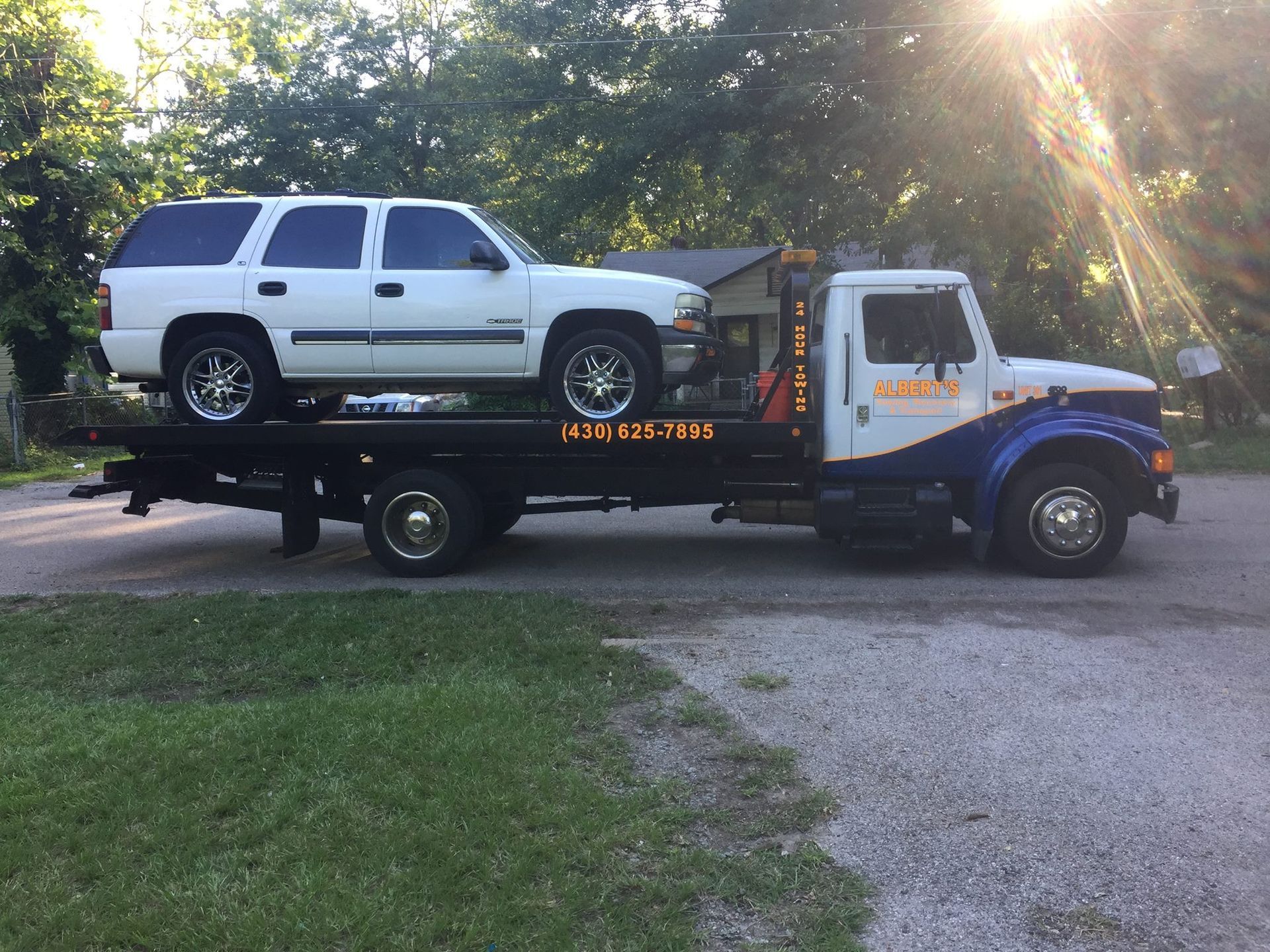 White SUV on a tow truck, parked on a driveway. Sun shining.