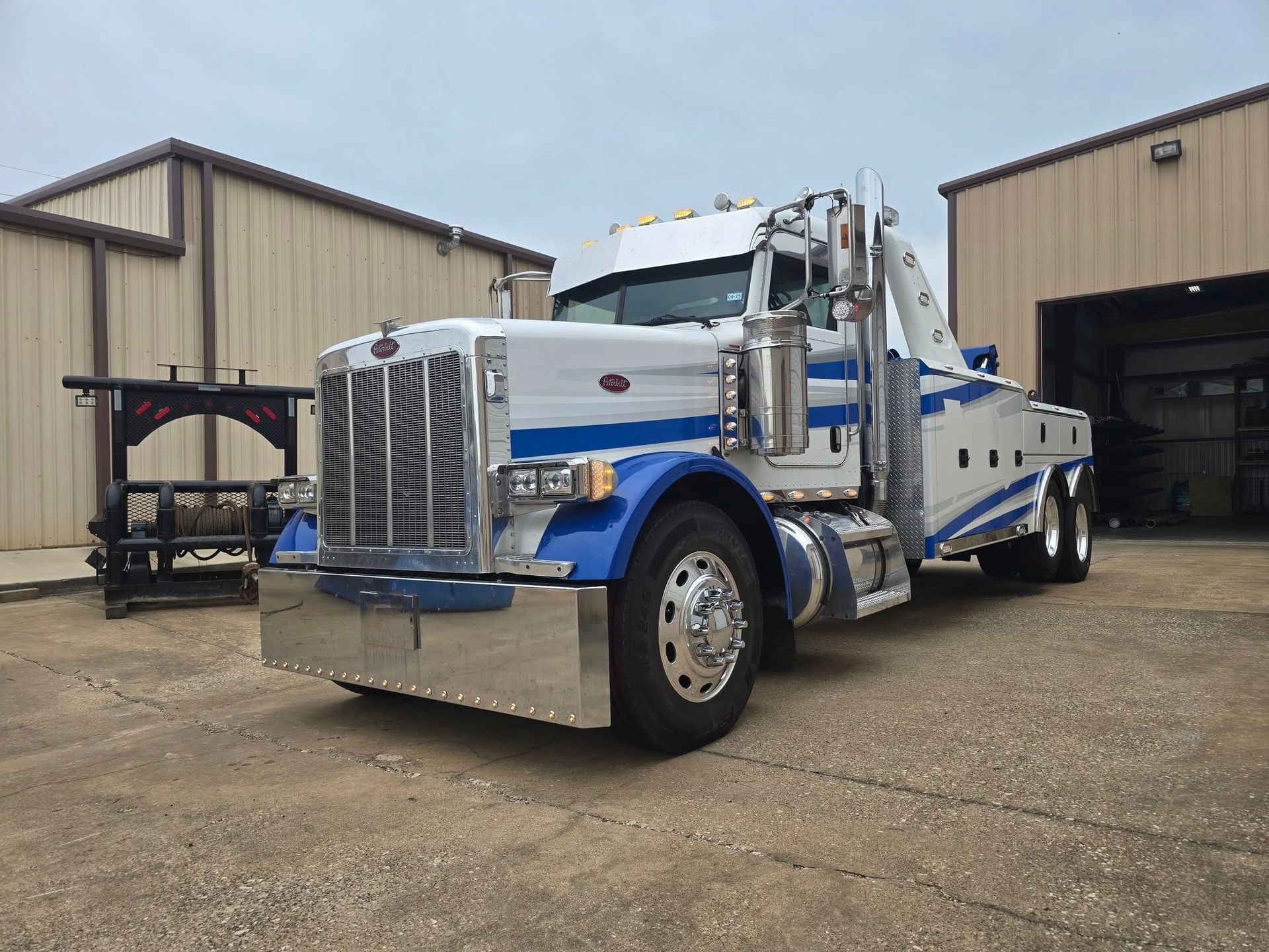 Silver and blue tow truck parked in front of a building with an open garage door.