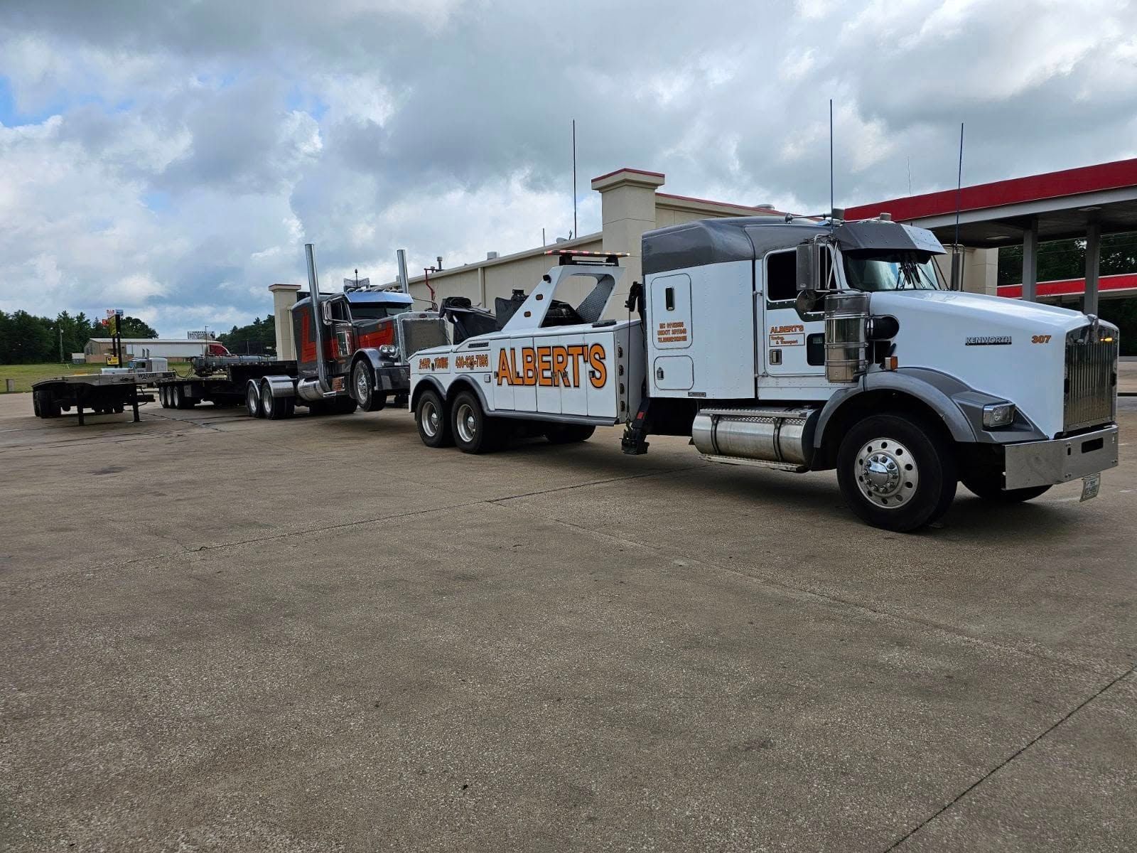 A white tow truck is towing a semi-truck with a flatbed trailer. 