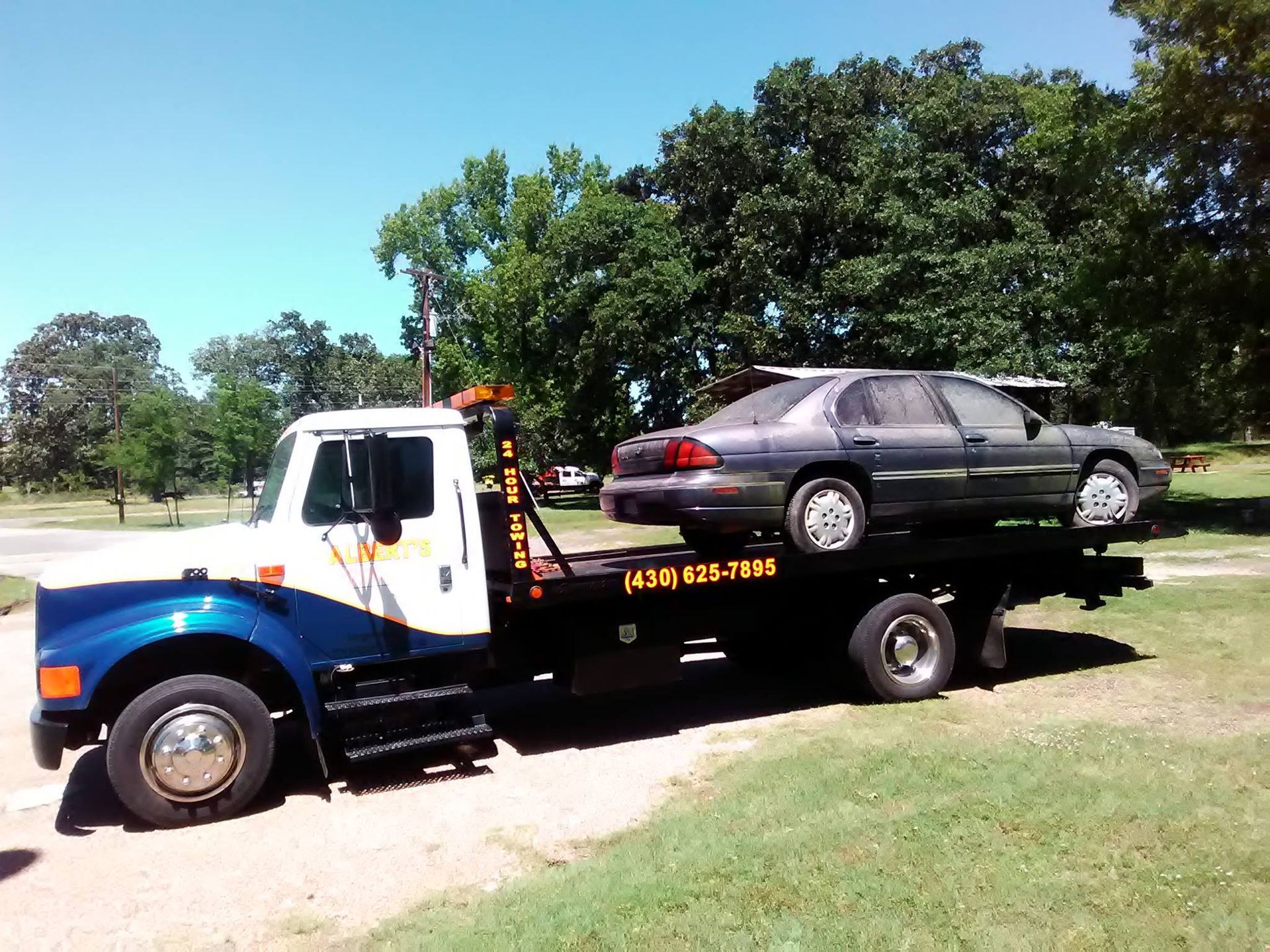 Tow truck hauling a gray car on a sunny day. The truck is white and blue.