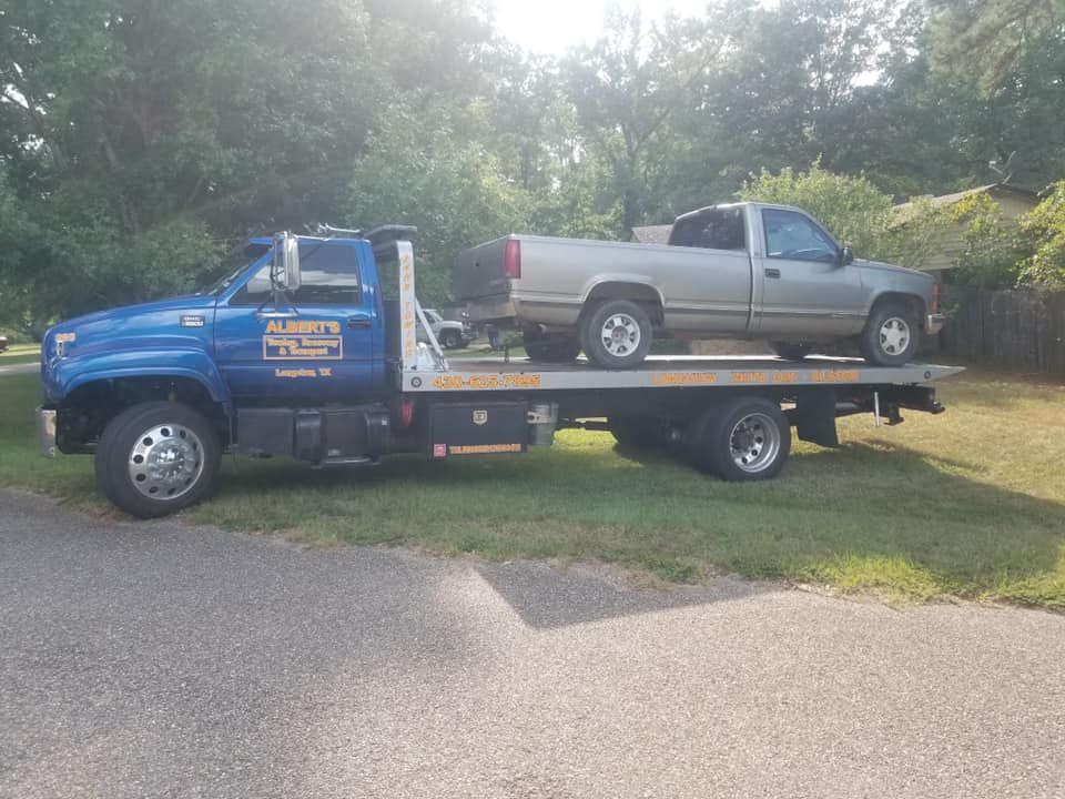 Blue tow truck carrying a silver pickup truck on a sunny day.