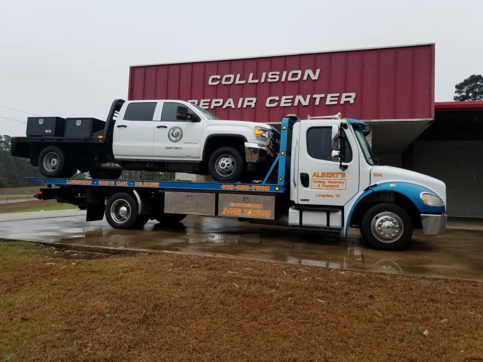 Tow truck carrying a white pickup truck in front of a collision repair center.