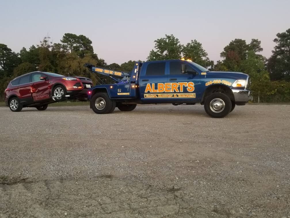Blue tow truck towing a red, damaged car in a parking lot. 