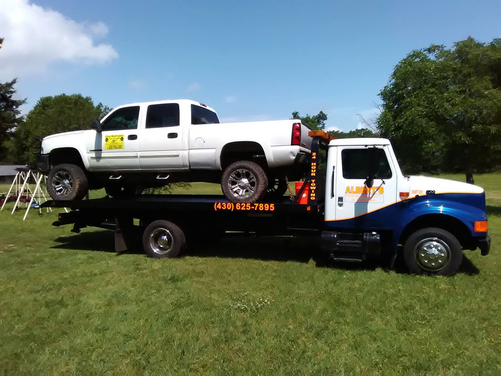 White pickup truck on a blue and white tow truck in a grassy area under a blue sky.