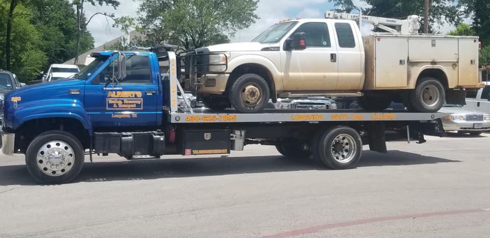 A blue tow truck hauling a white pickup truck on a sunny day.