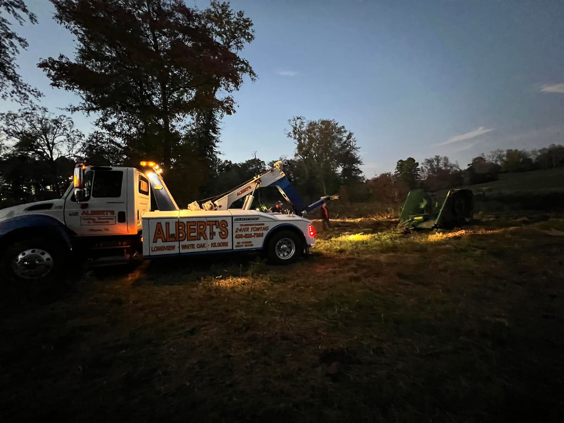 A tow truck from Albert's recovering a vehicle in a field at dusk.