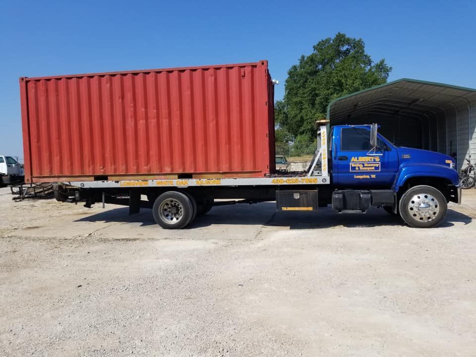 Blue truck carrying a large red shipping container on a sunny day.