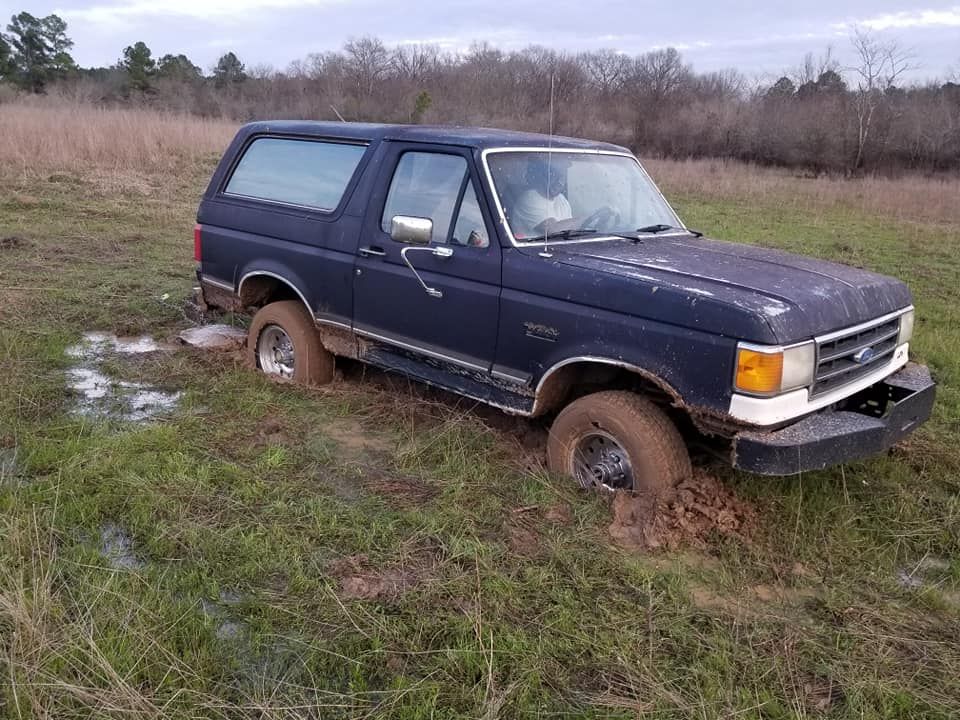 Dark blue Ford Bronco stuck in mud in a grassy field.