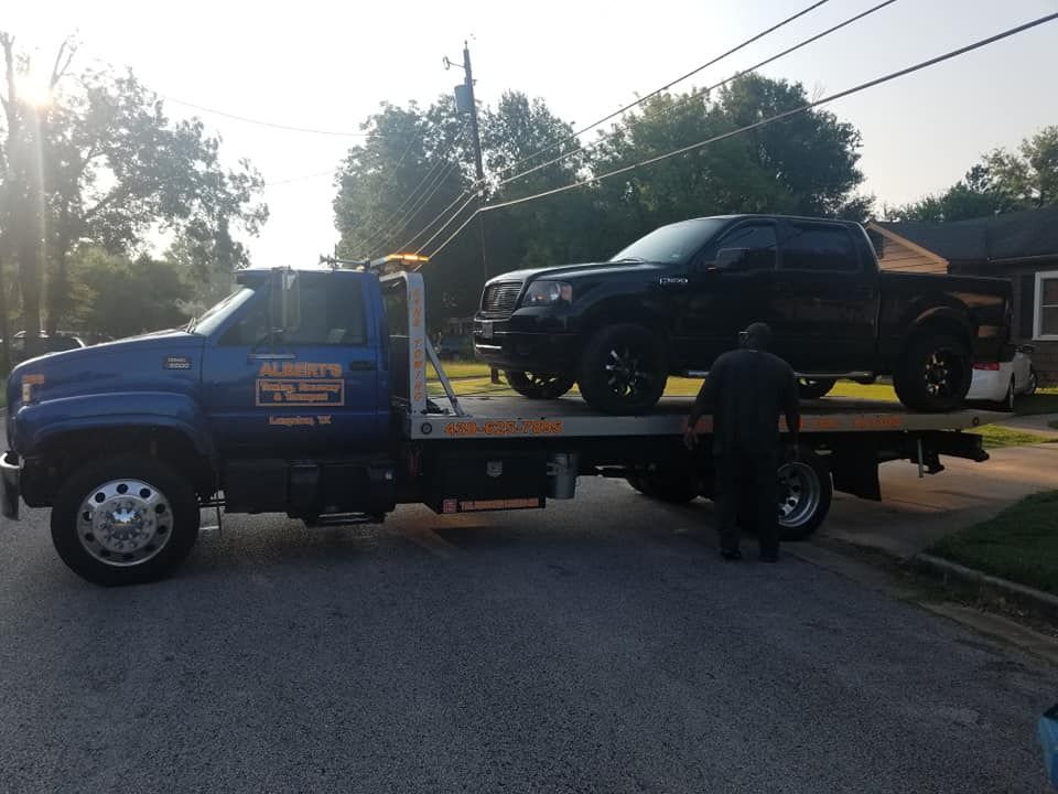 Tow truck loading a black pickup truck on a residential street.