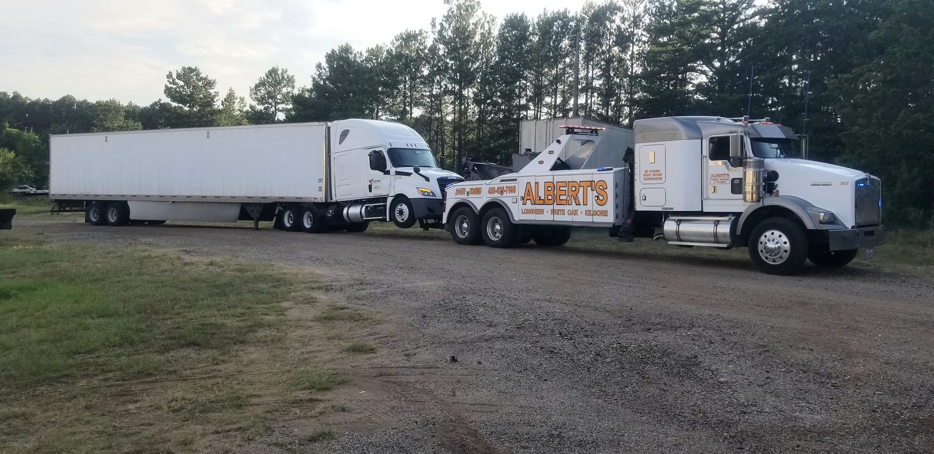 A tow truck pulling a white semi-truck. The tow truck reads