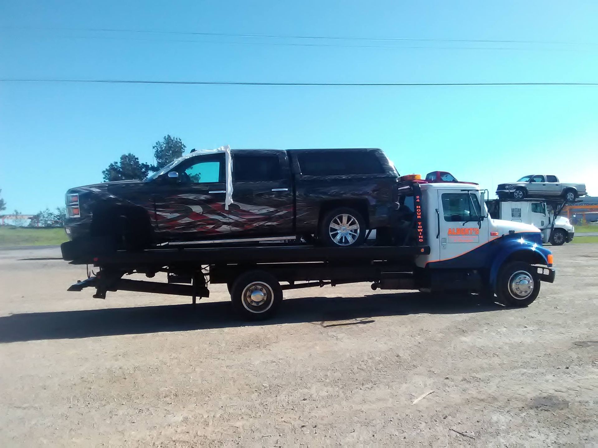 A tow truck carrying a damaged black pickup truck on a sunny day.
