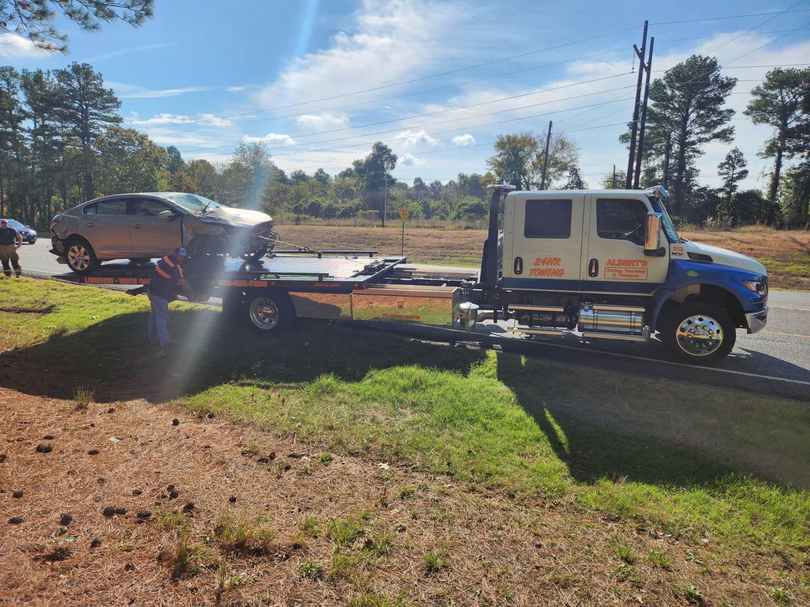 A gray car is being towed onto a flatbed truck on a roadside.