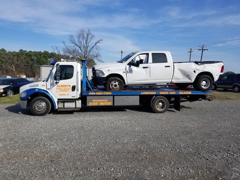Tow truck carrying a damaged white pickup truck on a sunny day.