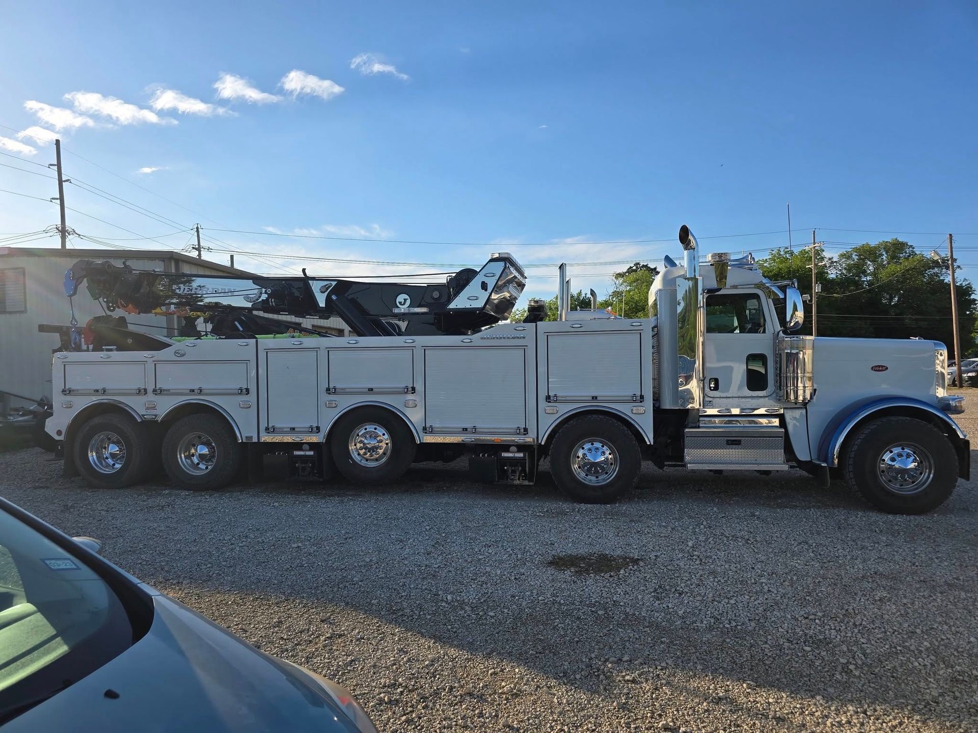 White heavy-duty tow truck parked on gravel lot under a blue sky.