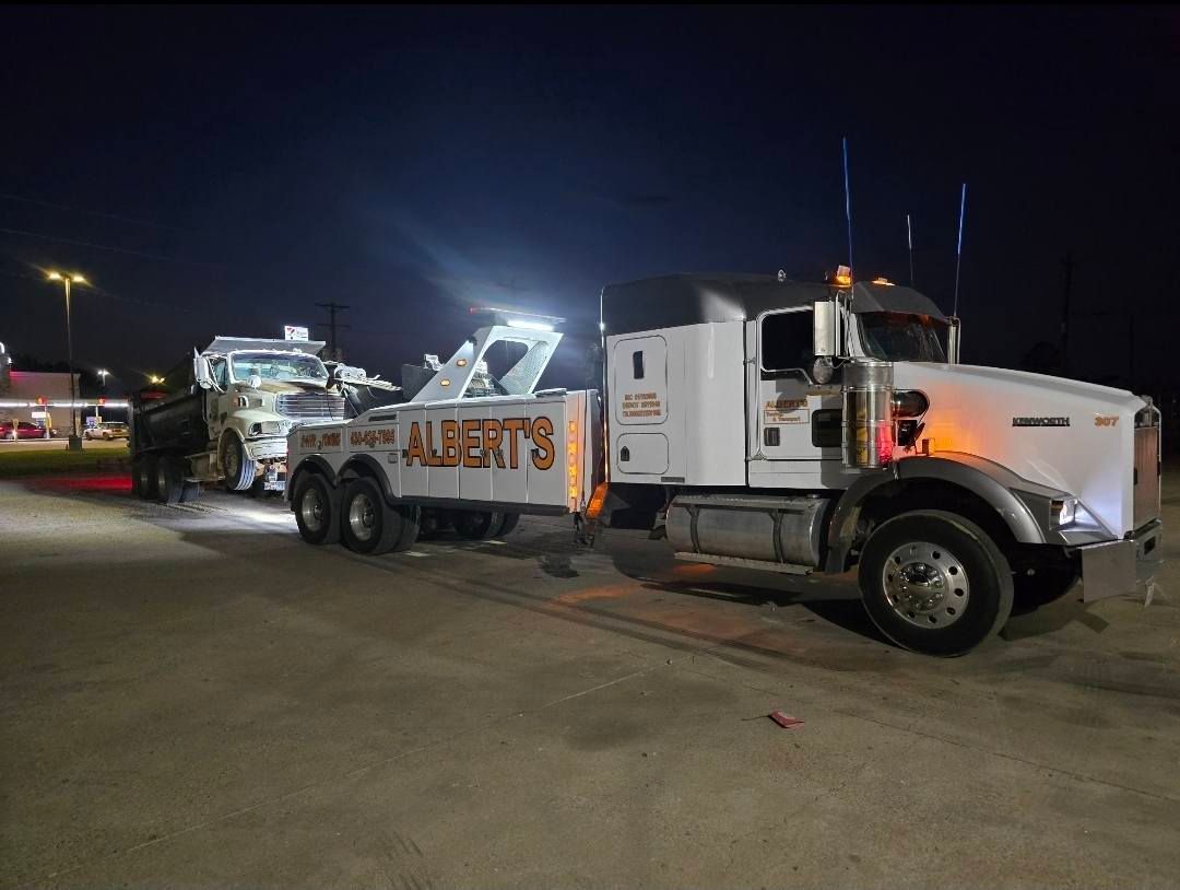 A tow truck with flashing lights towing another vehicle at night. The tow truck says 