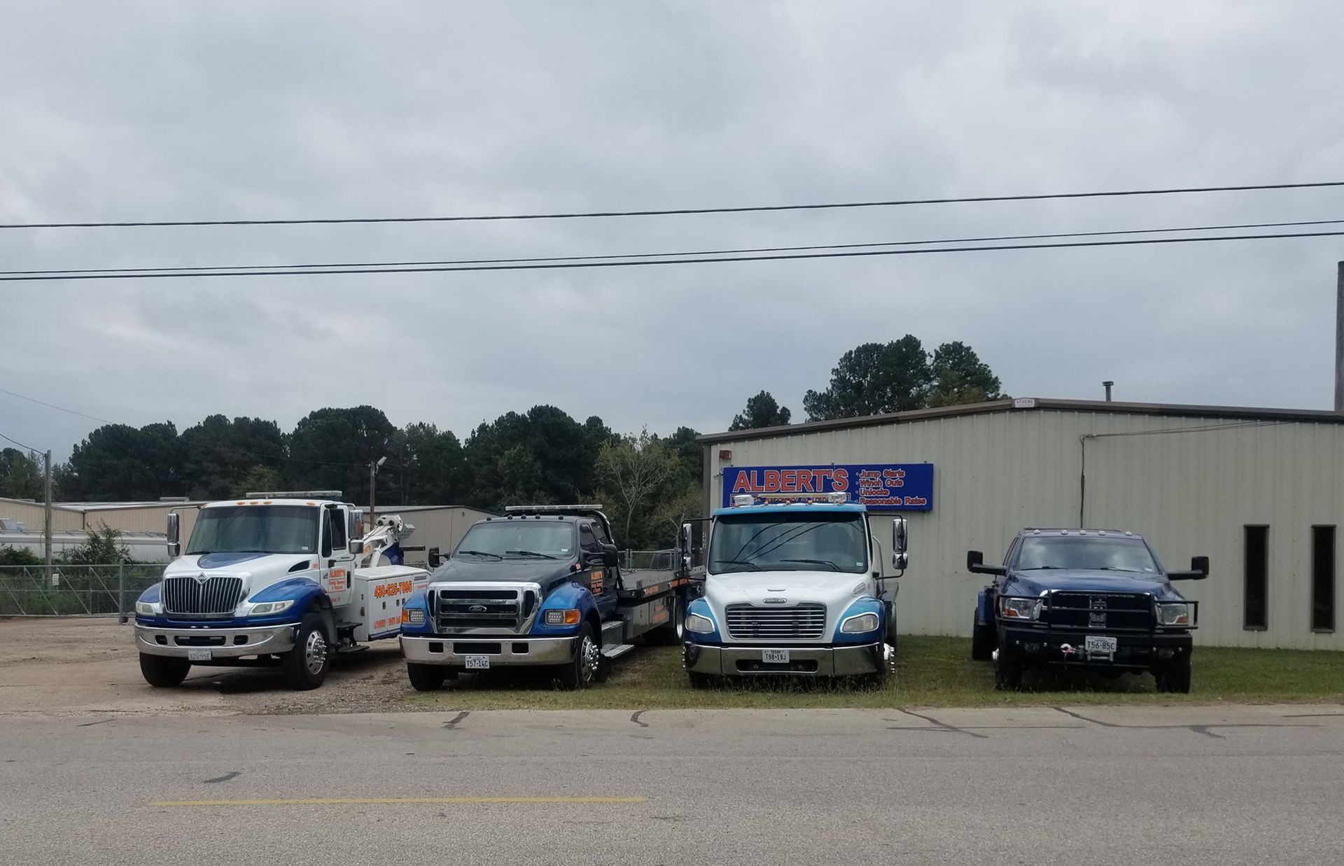 Four tow trucks parked in front of a business on a cloudy day.