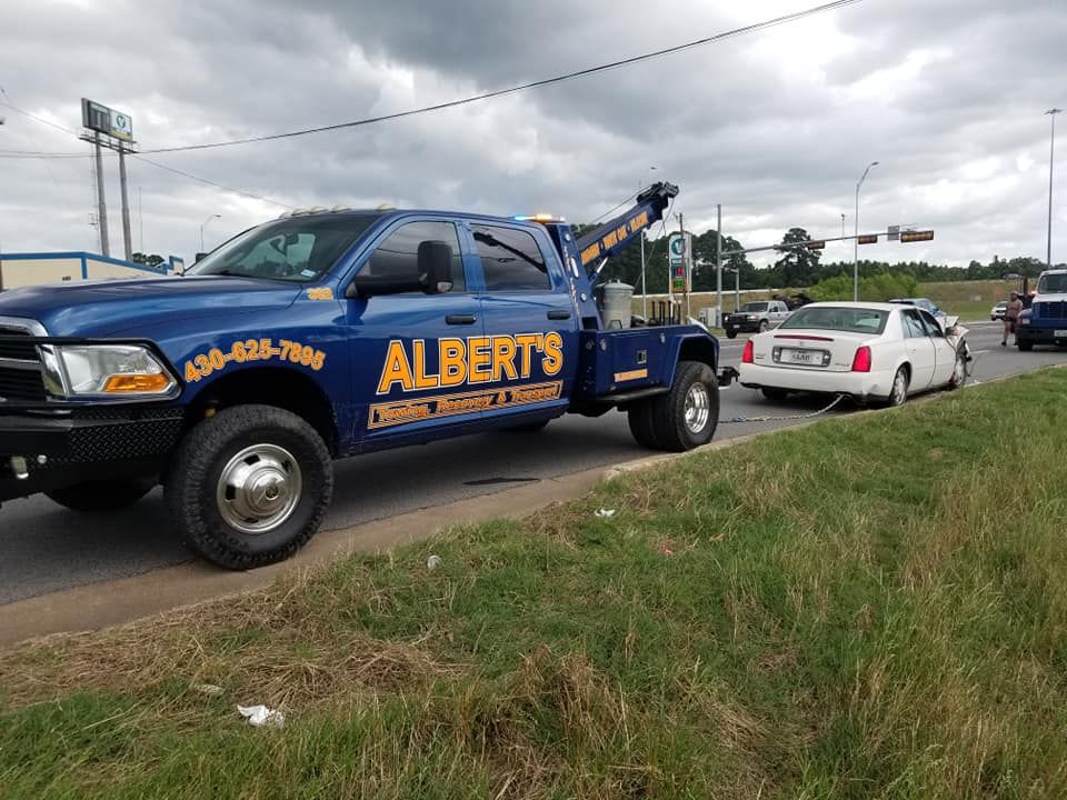 A blue Albert's Towing truck towing a white car on a roadside with green grass.