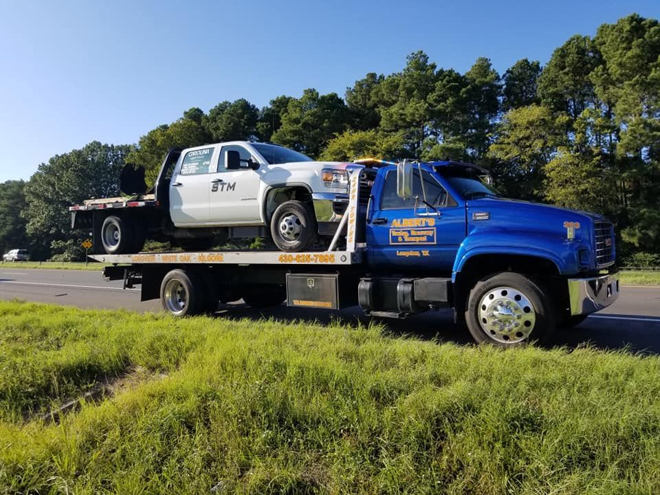 Blue tow truck carrying a white pickup truck on a highway.