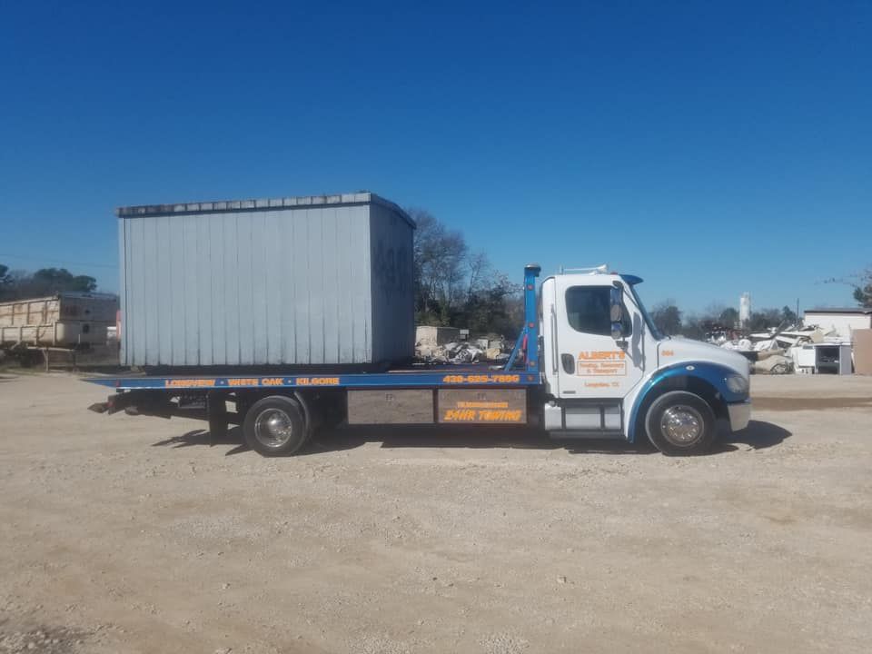 A flatbed tow truck carrying a large metal container under a clear blue sky.
