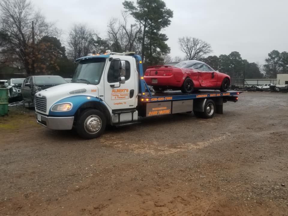 Tow truck hauling a damaged red sports car on a gravel lot under overcast skies.