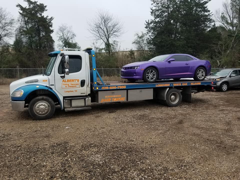 Tow truck transporting a purple sports car. Exterior setting, cloudy day.