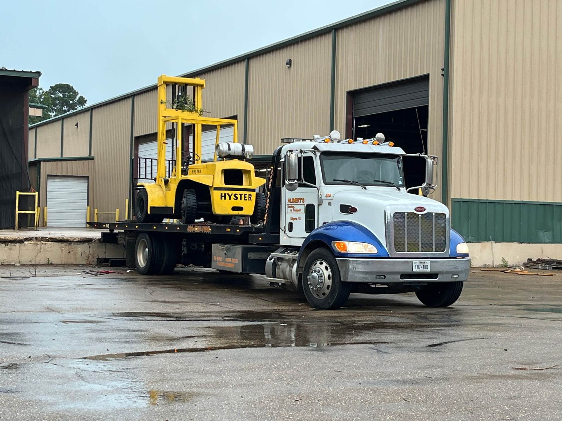 Yellow forklift on flatbed truck in front of a warehouse.