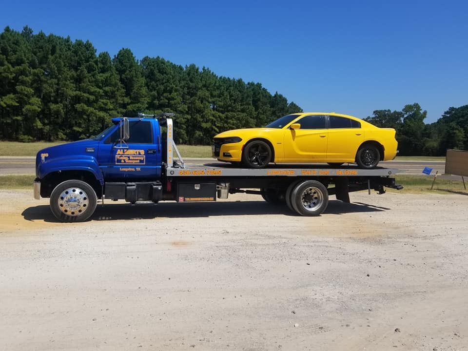 Blue tow truck with a yellow car on the flatbed, parked outside on a sunny day.