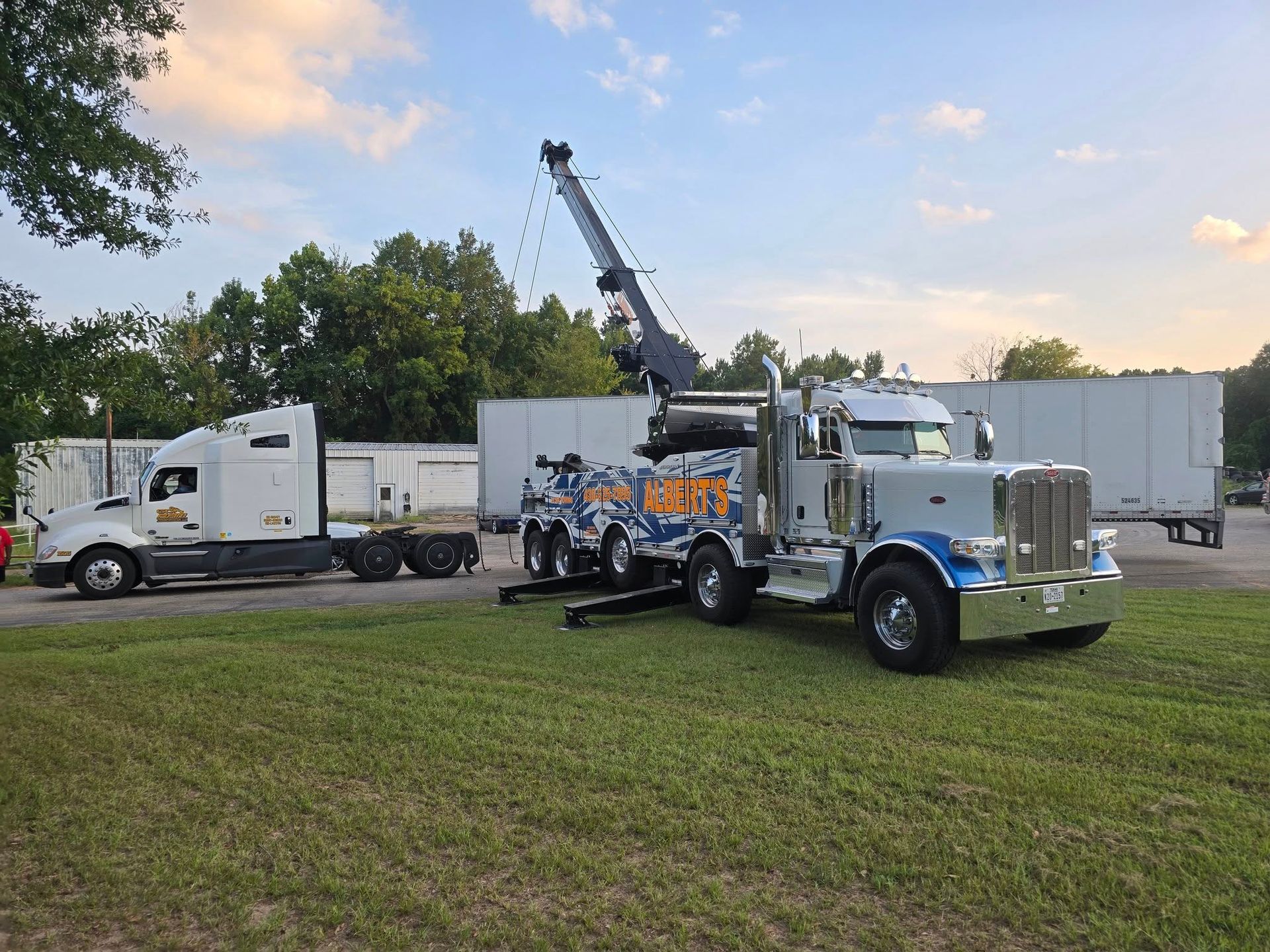 A tow truck preparing to haul a semi-truck in a grassy lot, under a cloudy sky.
