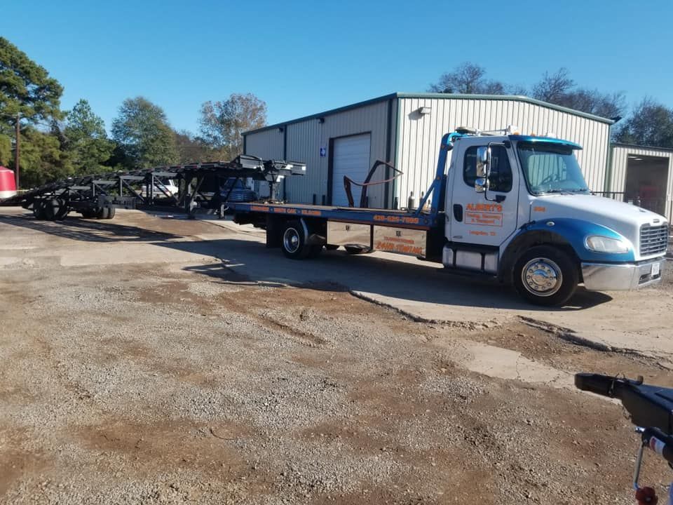 Tow truck in front of a warehouse. Blue and white truck, grey gravel, sunny day.