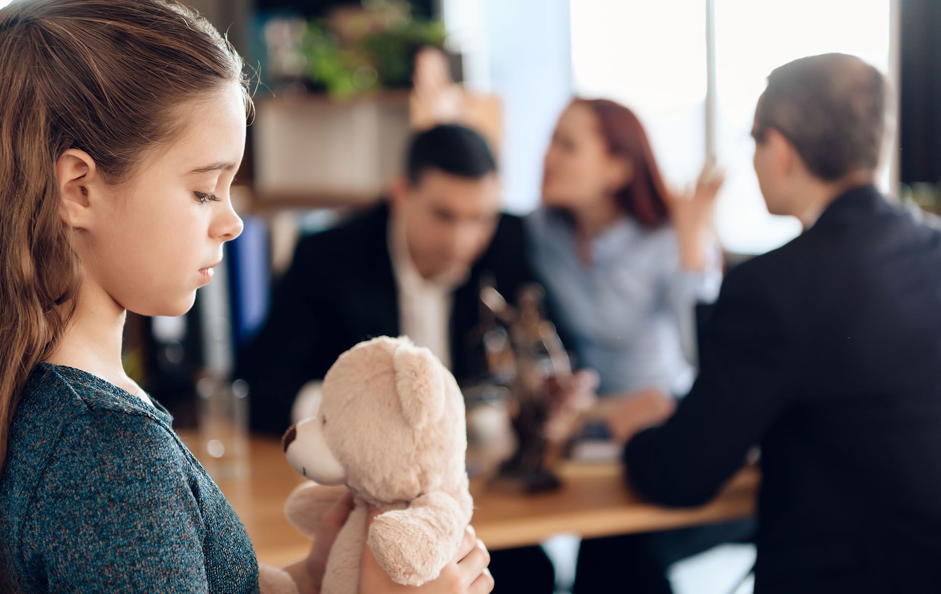 A little girl is holding a teddy bear in front of a family.
