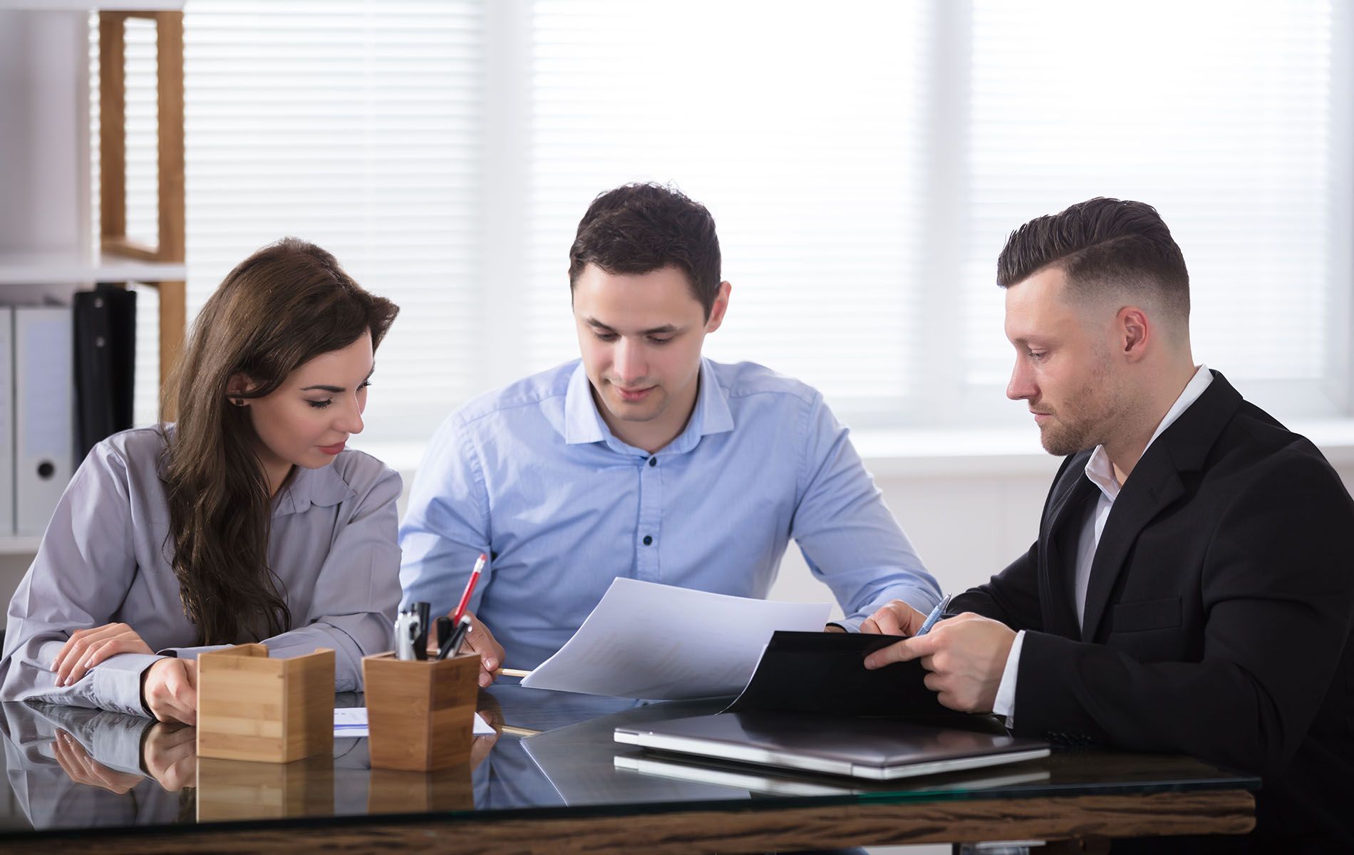 A group of people are sitting at a table looking at papers and a tablet.