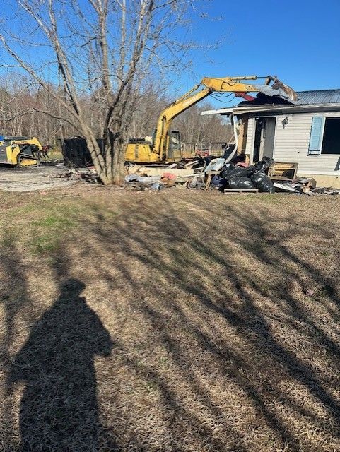 A house is being demolished by a yellow excavator.
