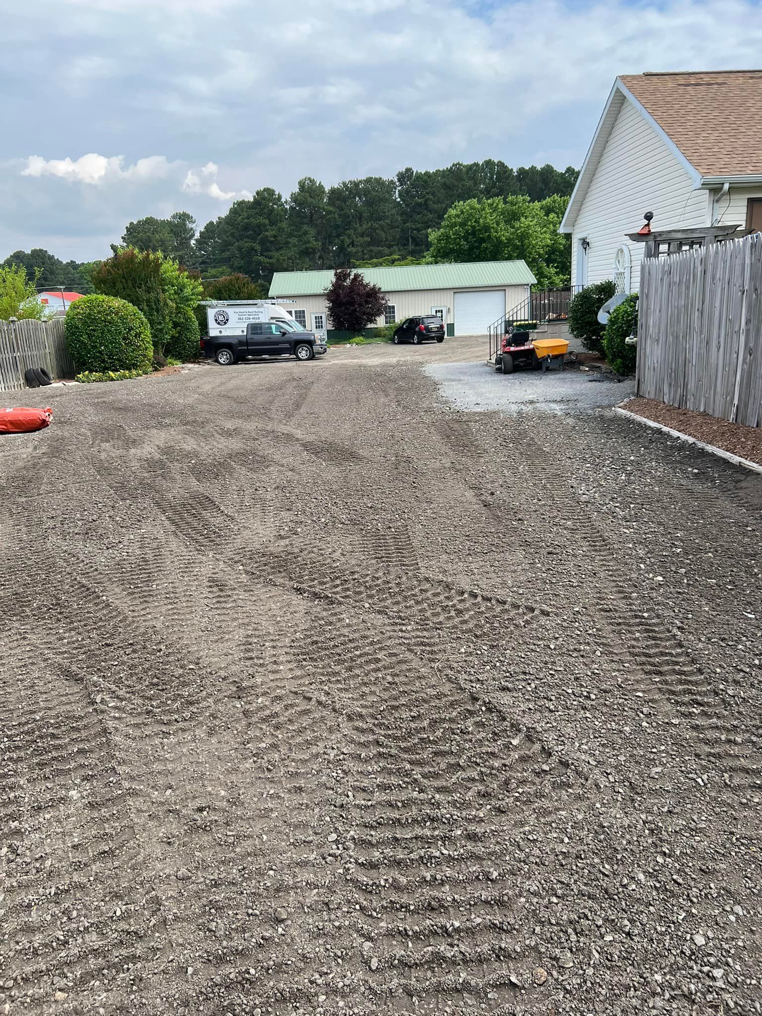 A gravel driveway with a fence and a house in the background.