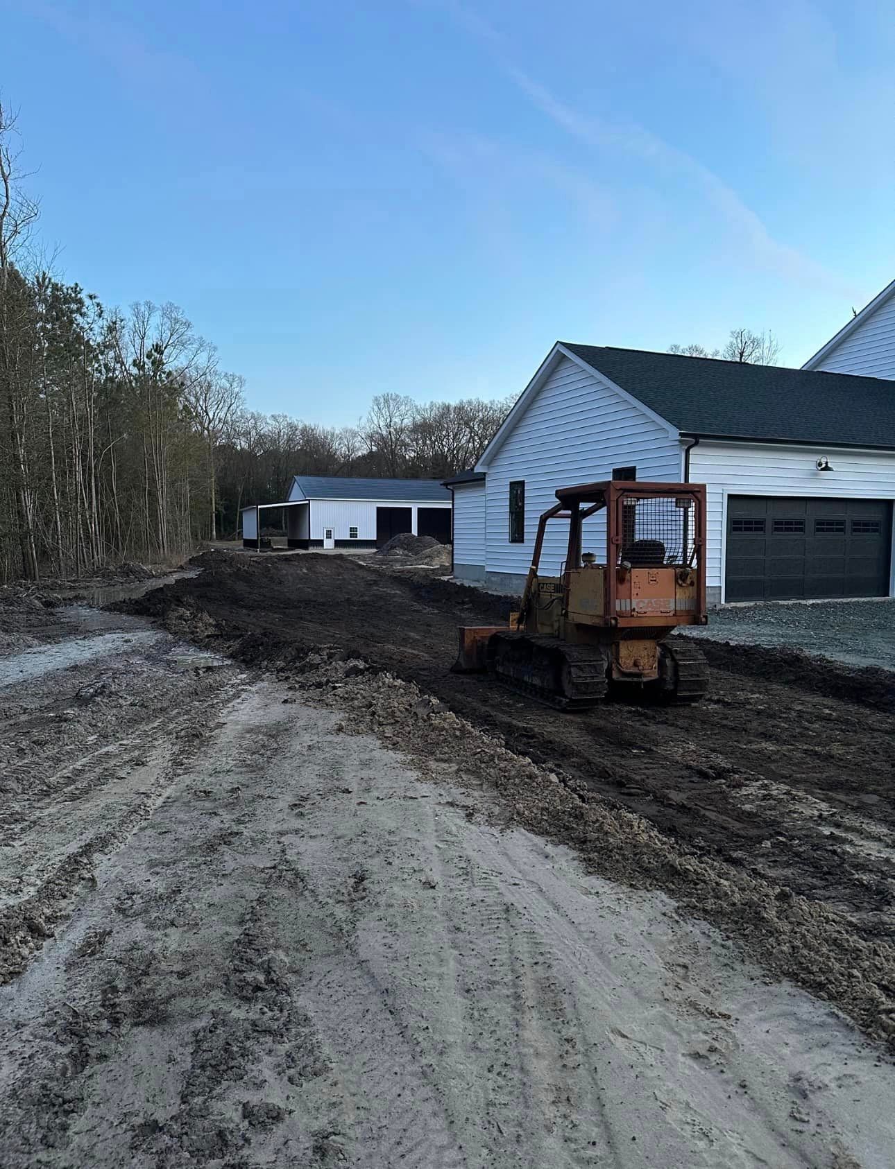A bulldozer is driving down a dirt road in front of a house.