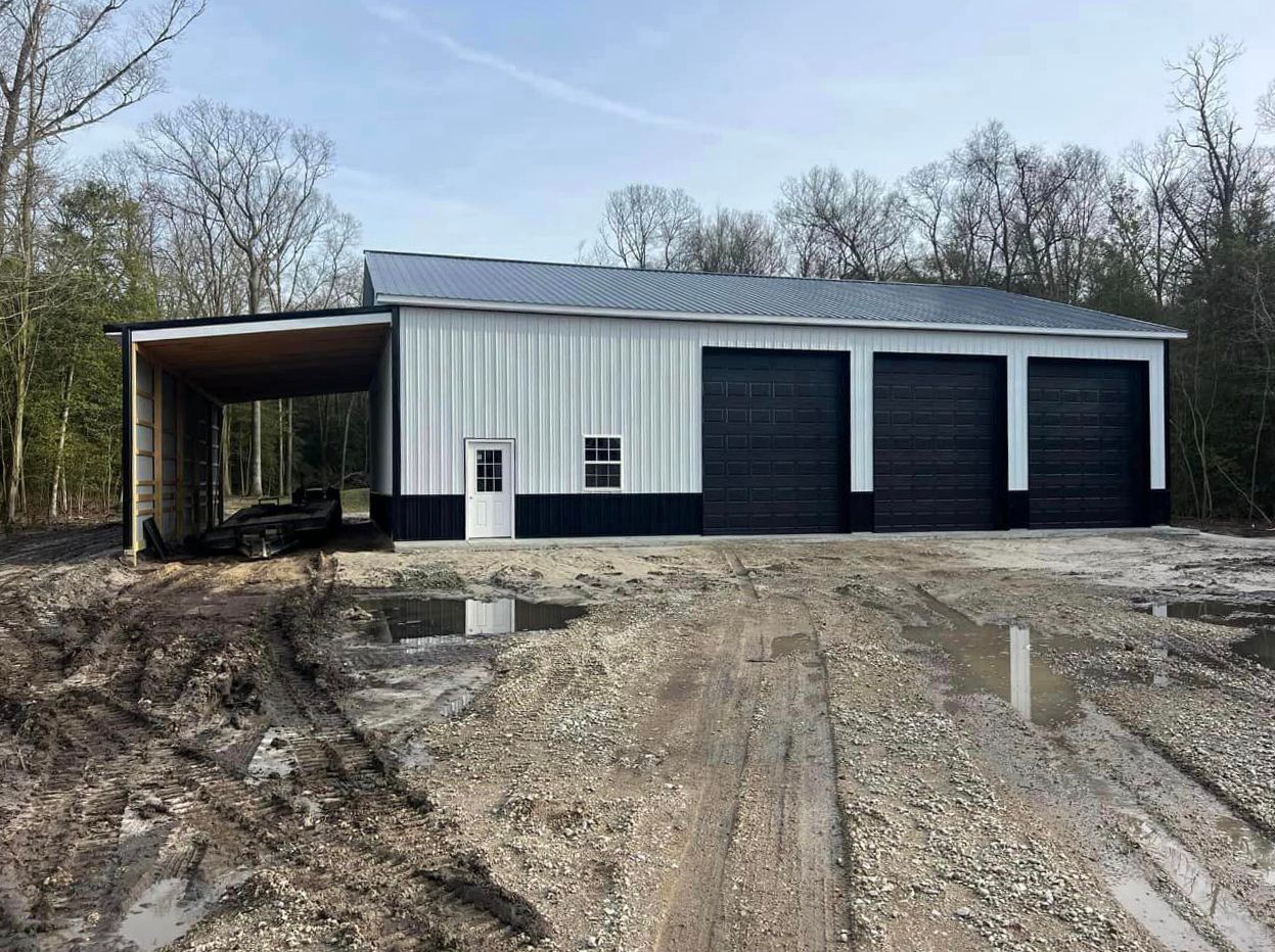 A white and black garage with three garage doors is sitting in the middle of a dirt road.