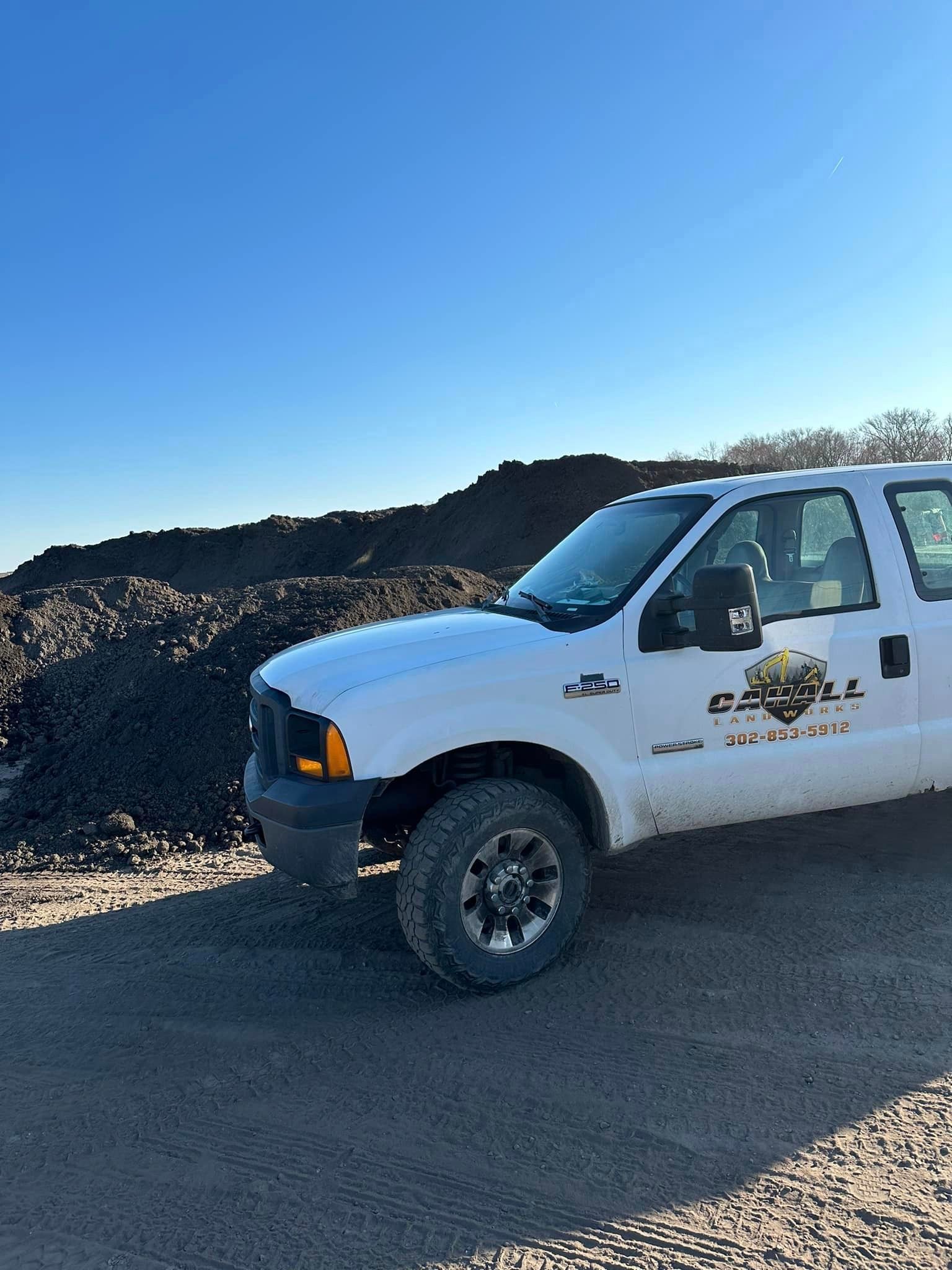 A white truck is parked on the side of a dirt road.