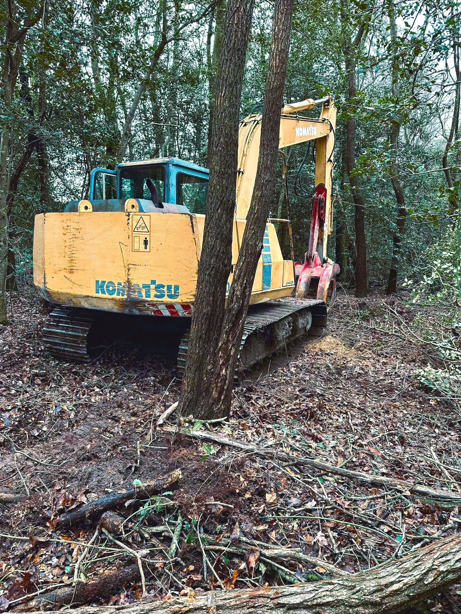 A yellow excavator is sitting in the middle of a forest.
