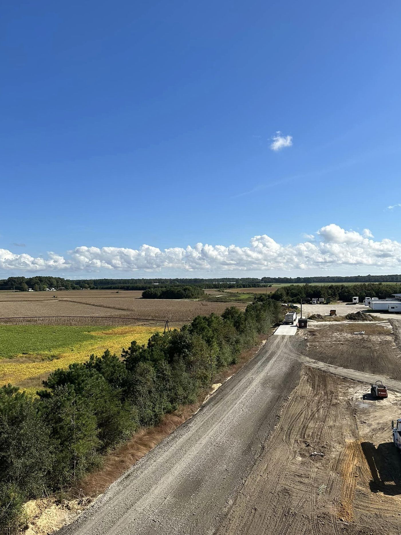A dirt road going through a field with a blue sky in the background.