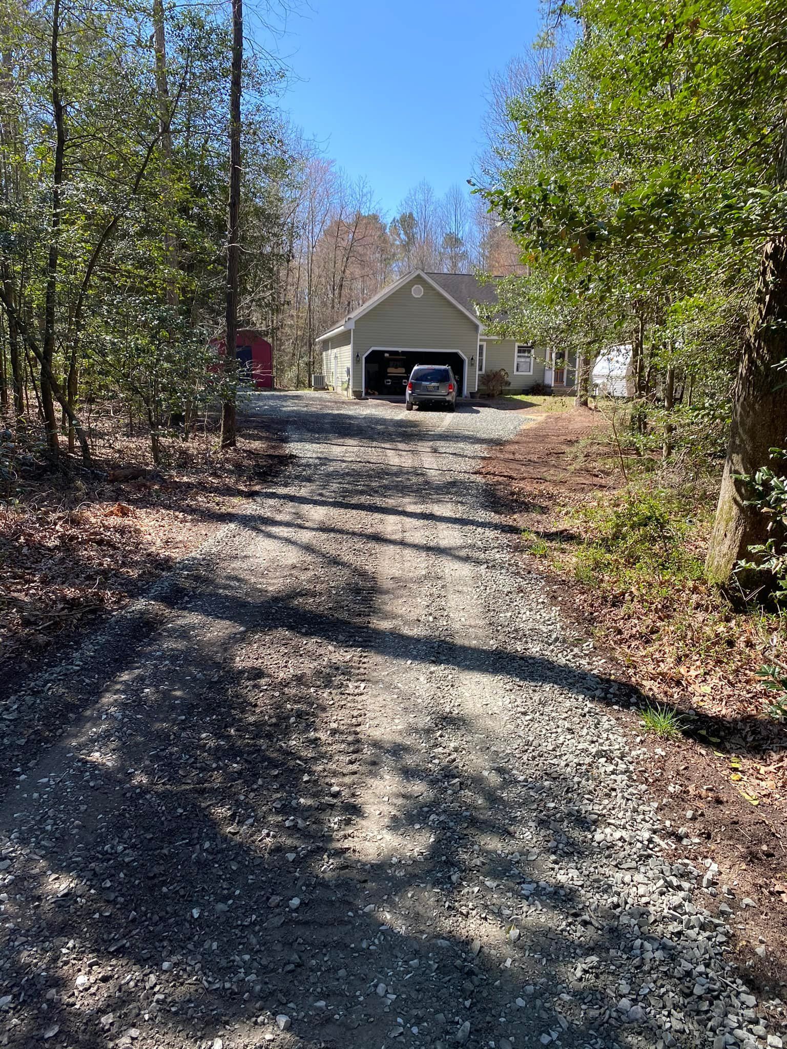 A dirt road leading to a house with a garage surrounded by trees.