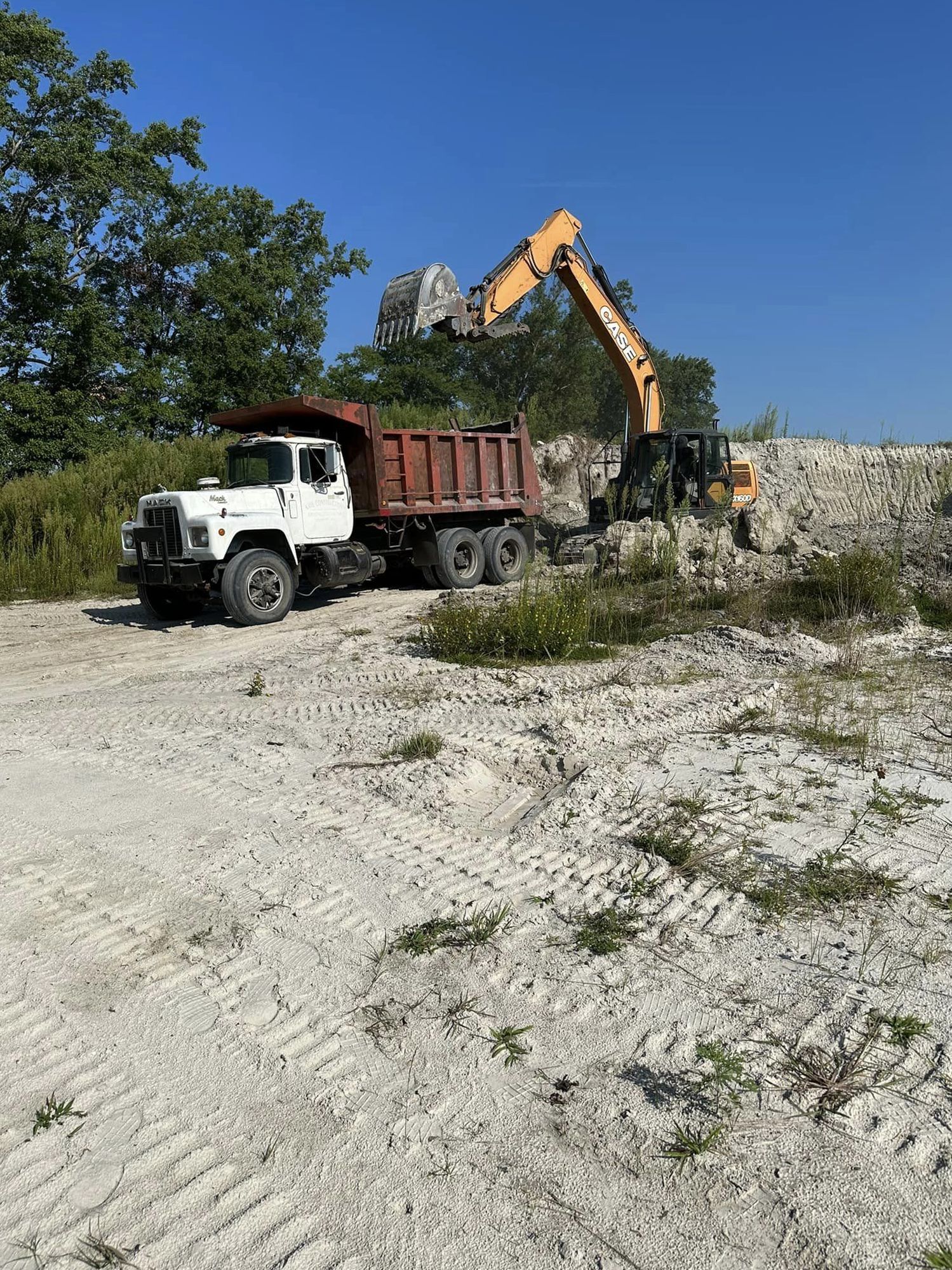 A dump truck is parked in a dirt lot next to an excavator.