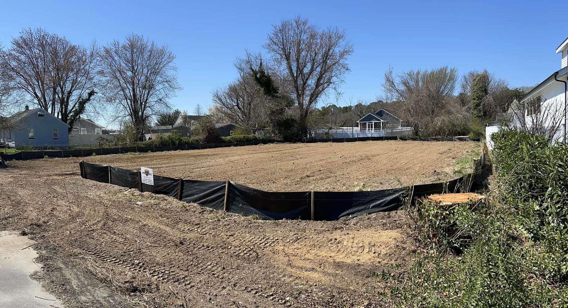 A large dirt field with a black fence around it and trees in the background.