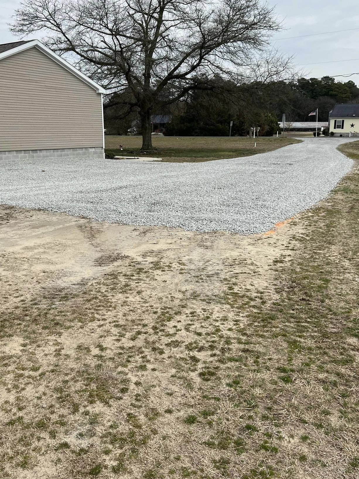 A gravel driveway leading to a house with a tree in the background.