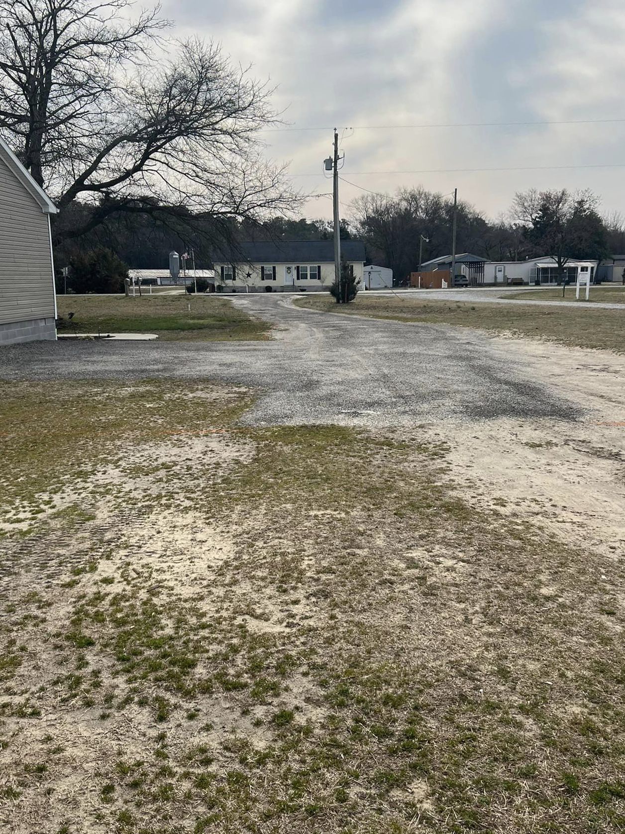 A dirt road going through a grassy field with a house in the background.