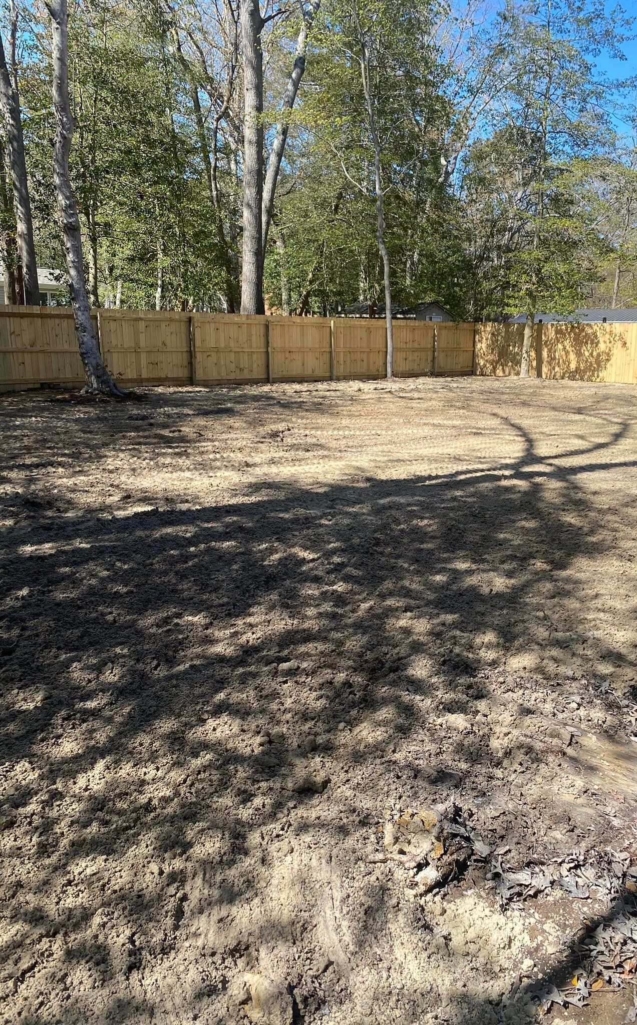 A dirt yard with a wooden fence and trees in the background.