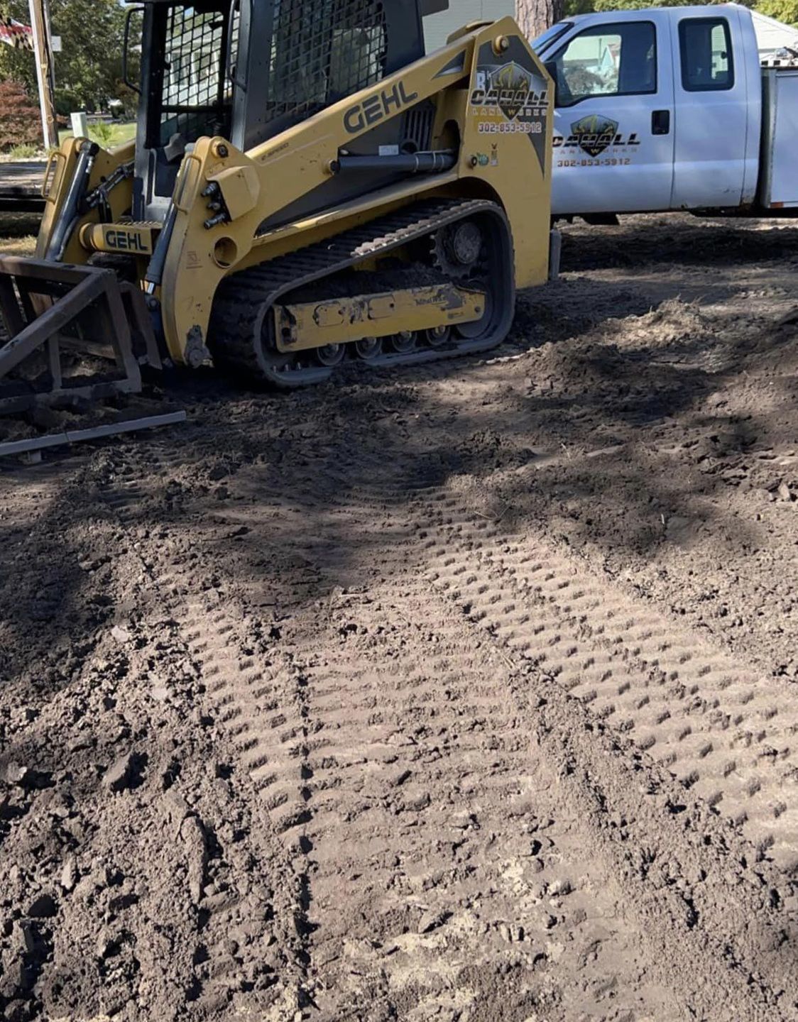 A yellow skid steer is parked next to a white truck